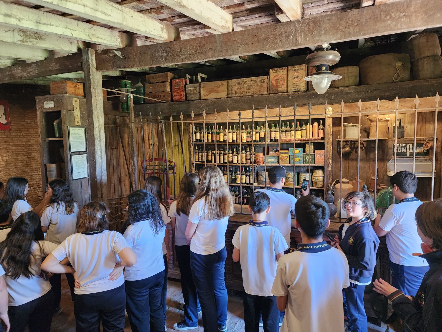 Visitantes en la sala de la pulpería entre estantes de madera y la reja del mostrador